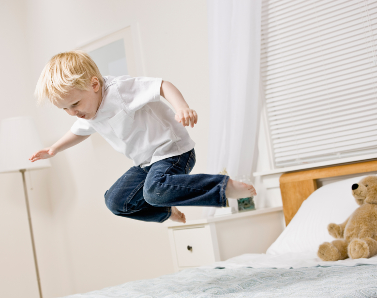Kleiner Junge springt auf einem Lattenrost und einer Matratze